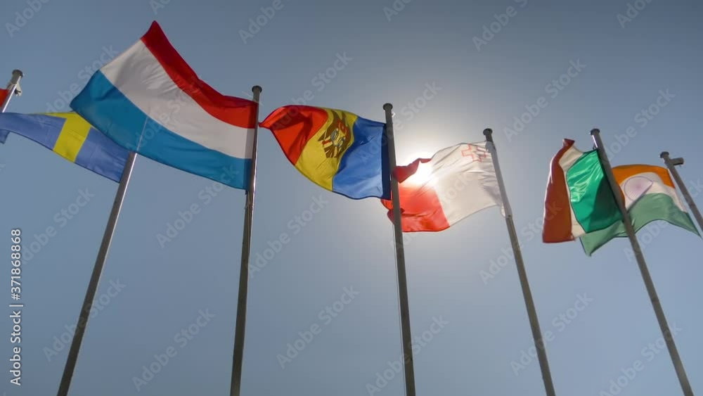 Super slow motion shot - colorful flags fluttering in the wind against blue sky. Summer day, sunny daylight, sun lens flare. Freedom, politics, patriotism, diplomacy and international affairs concept Super slow motion shot - colorful flags fluttering in the wind against blue sky. Summer day, sunny daylight, sun lens flare. Freedom, politics, patriotism, diplomacy and international affairs concept