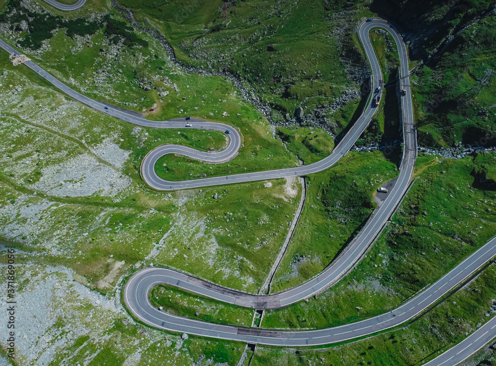 Above view of epic winding road on Transfagarasan pass in Romania in summer time, with twisty road rising up. Road crossing Fagaras mountain range. Vertical view.
