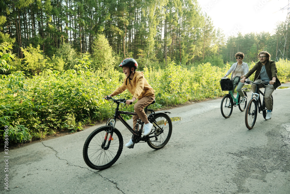 Young couple and their son riding bicycles along road in natural environment