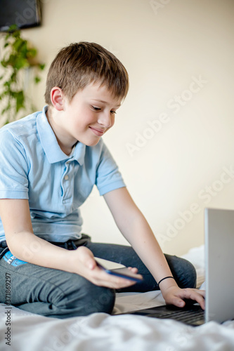 Smiling boy talking on laptop camera to communicate with foreign tuitor learning remotely through online class at home.