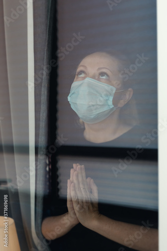 Quarantine woman in medical mask on face looking through the window.