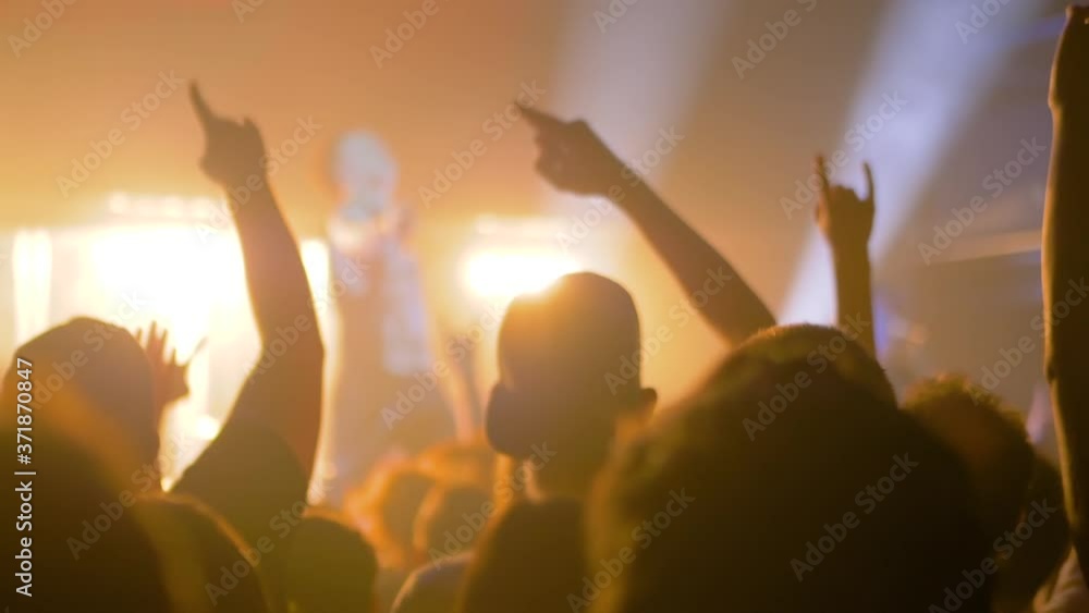 Super slow motion: people crowd partying, raising hands up, showing sign - devil's horns gesture and jumping at rock concert in front of stage of nightclub. Nightlife and entertainment concept Super slow motion: people crowd partying, raising hands up, showing sign - devil's horns gesture and jumping at rock concert in front of stage of nightclub. Nightlife and entertainment concept
