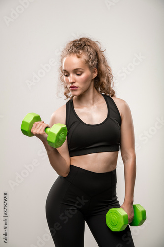 Fit girl in black sportswear holding green dumbbells in hands during workout