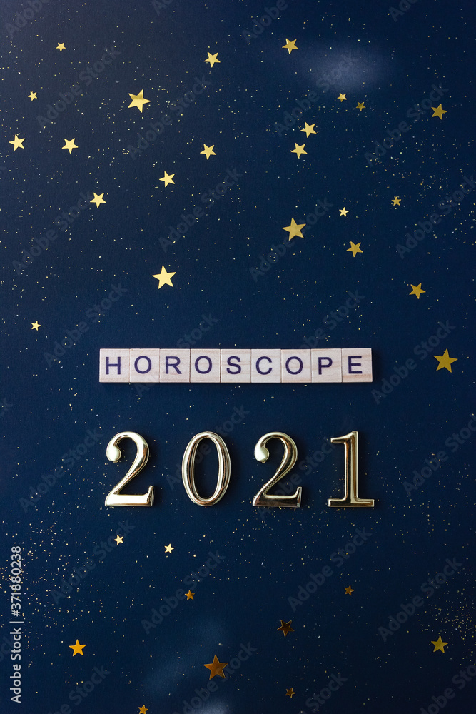 Word Horoscope and 2021 numbers. Wooden blocks with lettering on dark blue background decorated with stars confetti. Vertical flat lay.