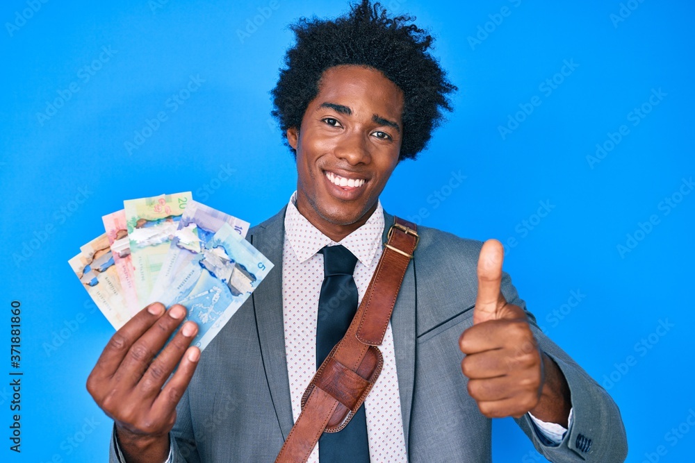 Handsome african american business man with afro hair holding canadian dollars smiling happy and positive, thumb up doing excellent and approval sign Handsome african american business man with afro hair holding canadian dollars smiling happy and positive, thumb up doing excellent and approval sign