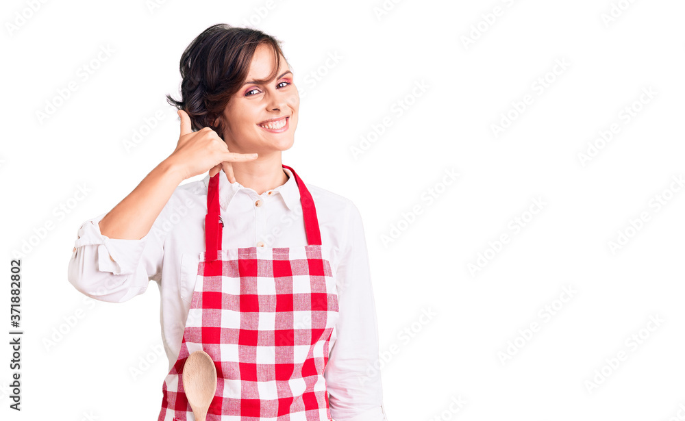 Beautiful young woman with short hair wearing professional cook apron smiling doing phone gesture with hand and fingers like talking on the telephone. communicating concepts. Beautiful young woman with short hair wearing professional cook apron smiling doing phone gesture with hand and fingers like talking on the telephone. communicating concepts.