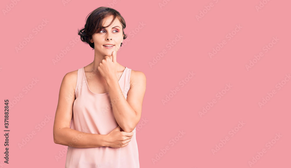 Beautiful young woman with short hair wearing casual style with sleeveless shirt with hand on chin thinking about question, pensive expression. smiling with thoughtful face. doubt concept. Beautiful young woman with short hair wearing casual style with sleeveless shirt with hand on chin thinking about question, pensive expression. smiling with thoughtful face. doubt concept.