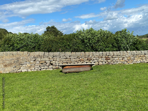 Old bath, in a field, used as a water trough, next to a dry stone wall, with trees, and a blue sky near, Farnley, Harrogate, UK photo