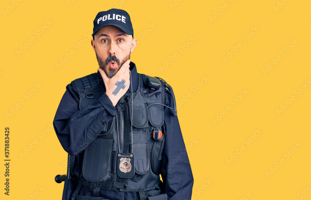 Fototapeta premium Young handsome man wearing police uniform looking fascinated with disbelief, surprise and amazed expression with hands on chin