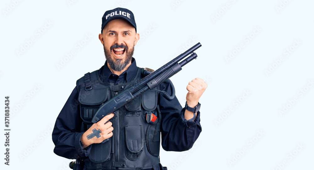 Young handsome man wearing police uniform holding shotgun screaming proud, celebrating victory and success very excited with raised arms Young handsome man wearing police uniform holding shotgun screaming proud, celebrating victory and success very excited with raised arms