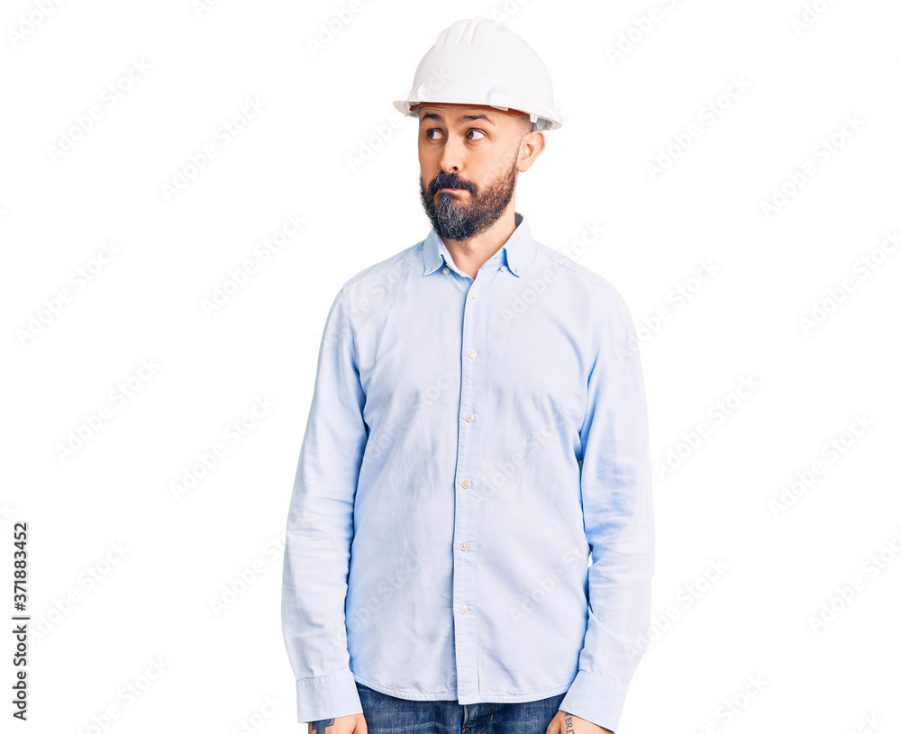 Young handsome man wearing architect hardhat smiling looking to the side and staring away thinking. Young handsome man wearing architect hardhat smiling looking to the side and staring away thinking.