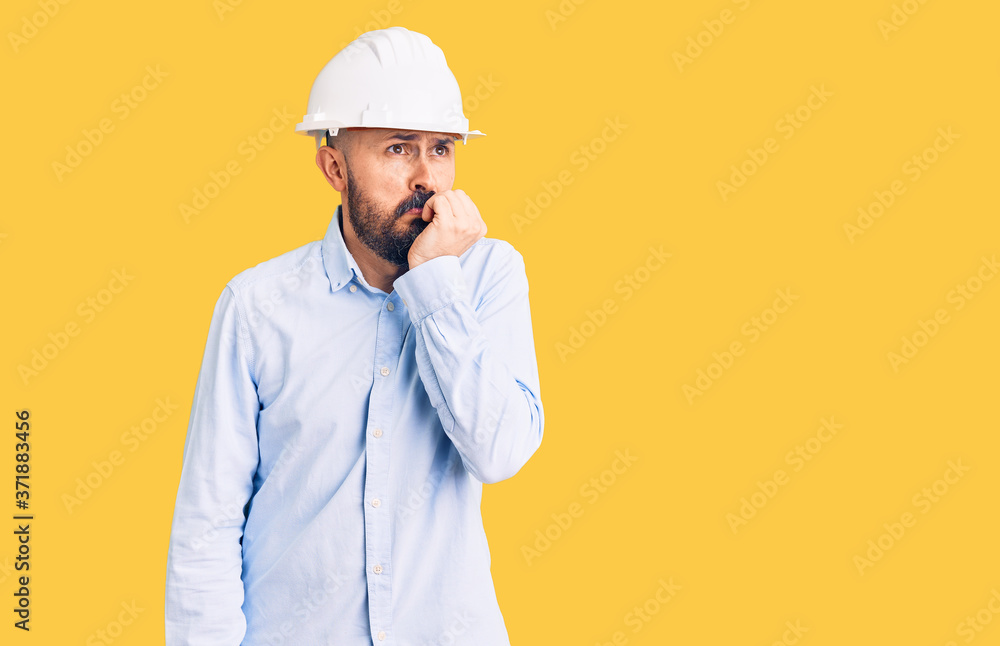 Young handsome man wearing architect hardhat looking stressed and nervous with hands on mouth biting nails. anxiety problem. Young handsome man wearing architect hardhat looking stressed and nervous with hands on mouth biting nails. anxiety problem.