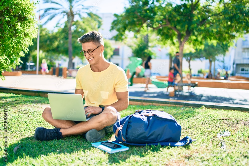 Obraz premium Young hispanic student smiling happy using laptop sitting on the grass at the university campus