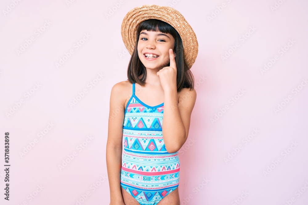 Young little girl with bang wearing swimsuit and summer hat smiling with an idea or question pointing finger up with happy face, number one Young little girl with bang wearing swimsuit and summer hat smiling with an idea or question pointing finger up with happy face, number one