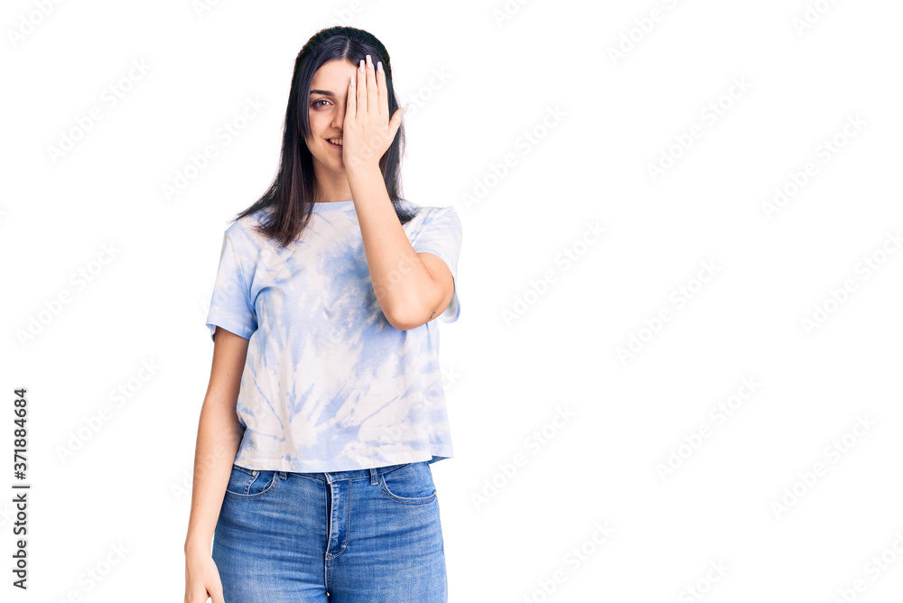 Young beautiful girl wearing casual t shirt covering one eye with hand, confident smile on face and surprise emotion. Young beautiful girl wearing casual t shirt covering one eye with hand, confident smile on face and surprise emotion.