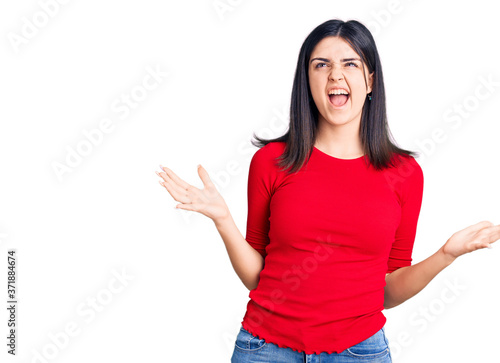 Young beautiful girl wearing casual t shirt crazy and mad shouting and yelling with aggressive expression and arms raised. frustration concept.