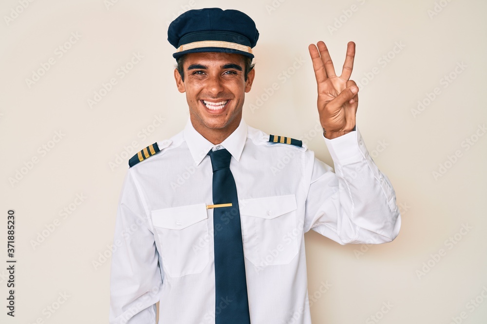 Young hispanic man wearing airplane pilot uniform showing and pointing up with fingers number three while smiling confident and happy. Young hispanic man wearing airplane pilot uniform showing and pointing up with fingers number three while smiling confident and happy.