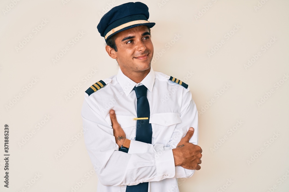 Young hispanic man wearing airplane pilot uniform looking to the side with arms crossed convinced and confident Young hispanic man wearing airplane pilot uniform looking to the side with arms crossed convinced and confident