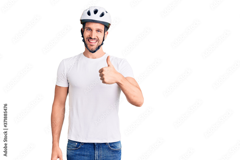 Young handsome man wearing bike helmet doing happy thumbs up gesture with hand. approving expression looking at the camera showing success. Young handsome man wearing bike helmet doing happy thumbs up gesture with hand. approving expression looking at the camera showing success.