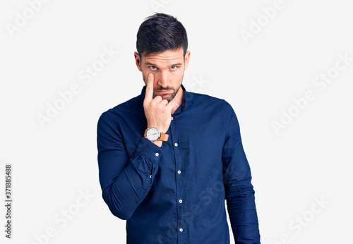 Young handsome man wearing casual shirt pointing to the eye watching you gesture, suspicious expression