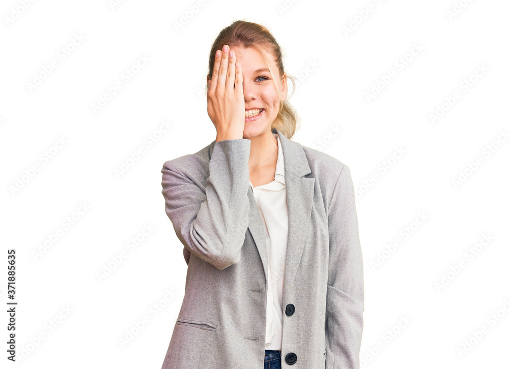 Young beautiful blonde woman wearing elegant jacket covering one eye with hand, confident smile on face and surprise emotion. Young beautiful blonde woman wearing elegant jacket covering one eye with hand, confident smile on face and surprise emotion.