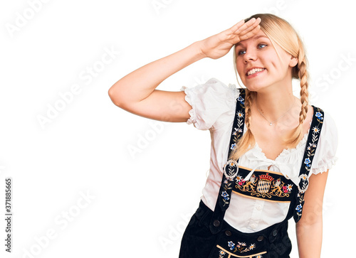 Young beautiful blonde woman wearing oktoberfest dress very happy and smiling looking far away with hand over head. searching concept. photo