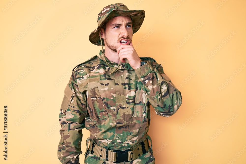 Young caucasian man wearing camouflage army uniform thinking worried about a question, concerned and nervous with hand on chin Young caucasian man wearing camouflage army uniform thinking worried about a question, concerned and nervous with hand on chin