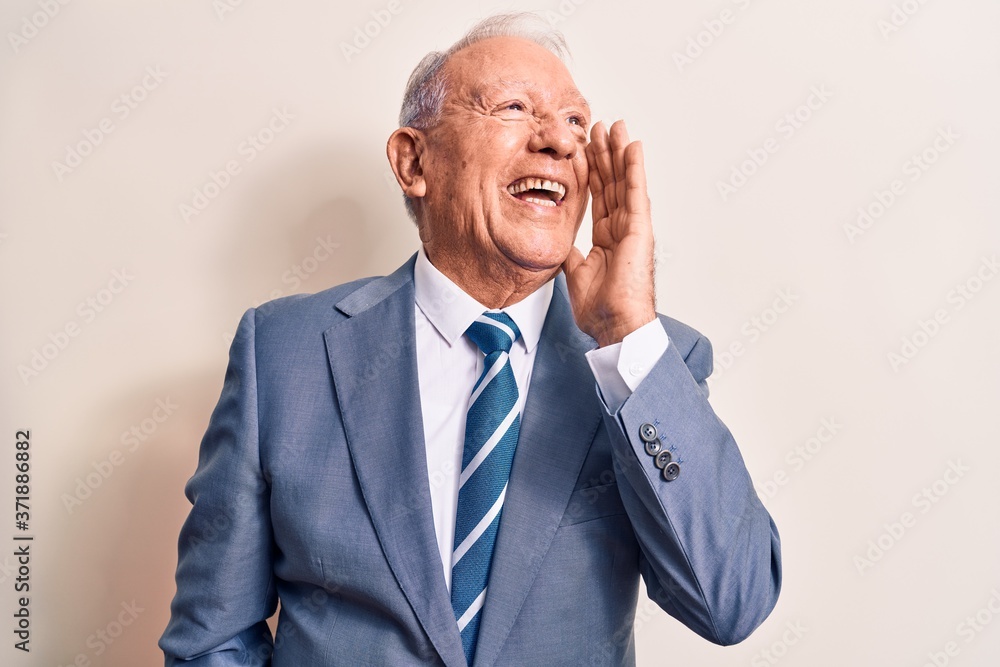 Senior handsome grey-haired businessman wearing elegant suit over white background shouting and screaming loud to side with hand on mouth. Communication concept. Senior handsome grey-haired businessman wearing elegant suit over white background shouting and screaming loud to side with hand on mouth. Communication concept.