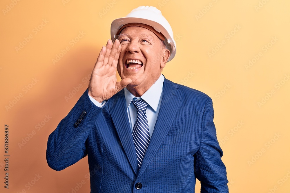 Senior grey-haired architect man wearing suit and security hardhat over yellow background shouting and screaming loud to side with hand on mouth. Communication concept. Senior grey-haired architect man wearing suit and security hardhat over yellow background shouting and screaming loud to side with hand on mouth. Communication concept.