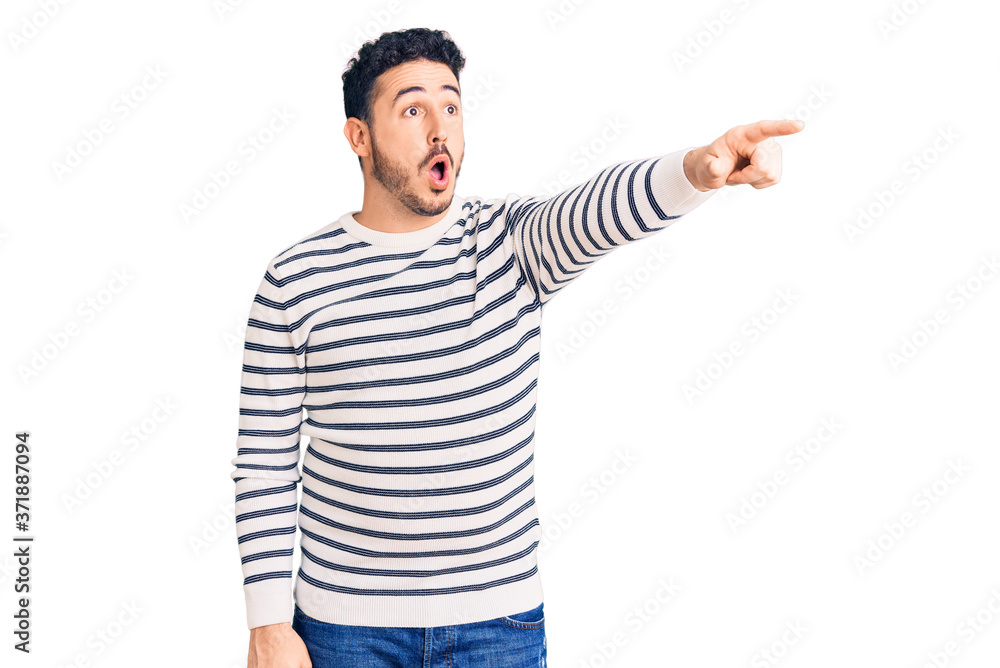 Young hispanic man wearing casual clothes pointing with finger surprised ahead, open mouth amazed expression, something on the front Young hispanic man wearing casual clothes pointing with finger surprised ahead, open mouth amazed expression, something on the front