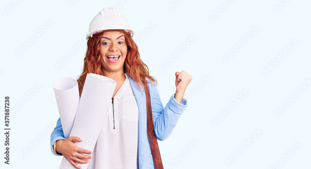 Young latin woman wearing architect hardhat and leather bag holding blueprints screaming proud, celebrating victory and success very excited with raised arms Young latin woman wearing architect hardhat and leather bag holding blueprints screaming proud, celebrating victory and success very excited with raised arms