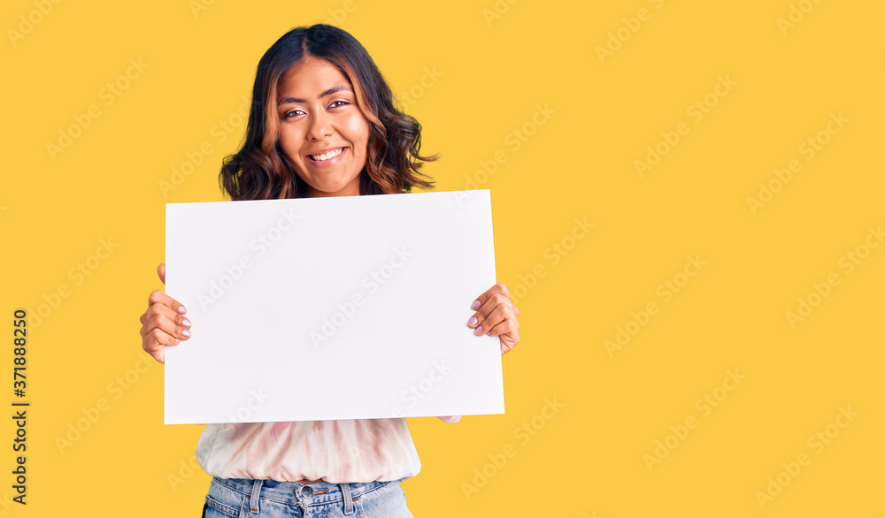 Young beautiful mixed race woman holding cardboard banner with blank space looking positive and happy standing and smiling with a confident smile showing teeth