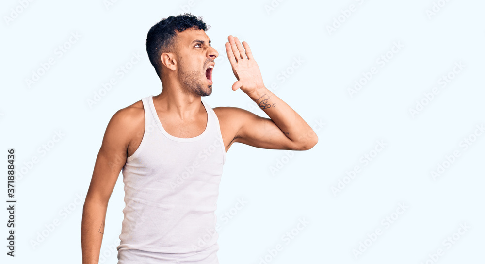 Young hispanic man wearing casual clothes shouting and screaming loud to side with hand on mouth. communication concept. Young hispanic man wearing casual clothes shouting and screaming loud to side with hand on mouth. communication concept.