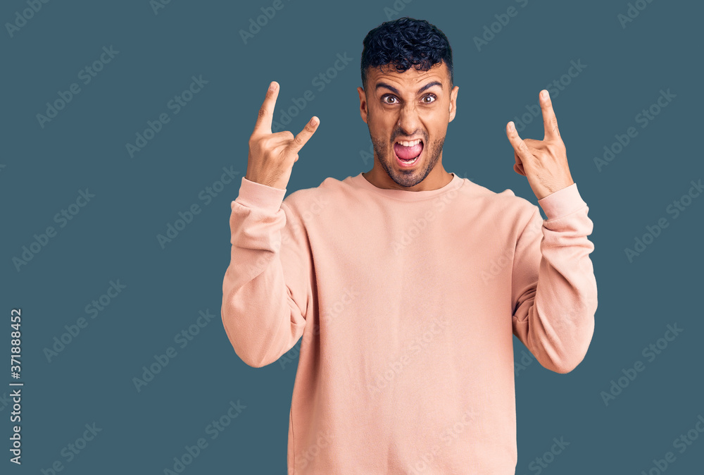 Young hispanic man wearing casual clothes shouting with crazy expression doing rock symbol with hands up. music star. heavy music concept. Young hispanic man wearing casual clothes shouting with crazy expression doing rock symbol with hands up. music star. heavy music concept.