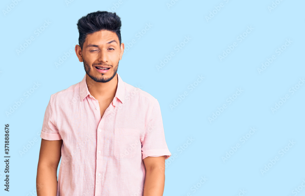 Handsome latin american young man wearing casual summer shirt winking looking at the camera with sexy expression, cheerful and happy face. Handsome latin american young man wearing casual summer shirt winking looking at the camera with sexy expression, cheerful and happy face.