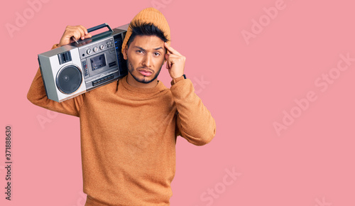 Handsome latin american young man holding boombox, listening to music worried and stressed about a problem with hand on forehead, nervous and anxious for crisis