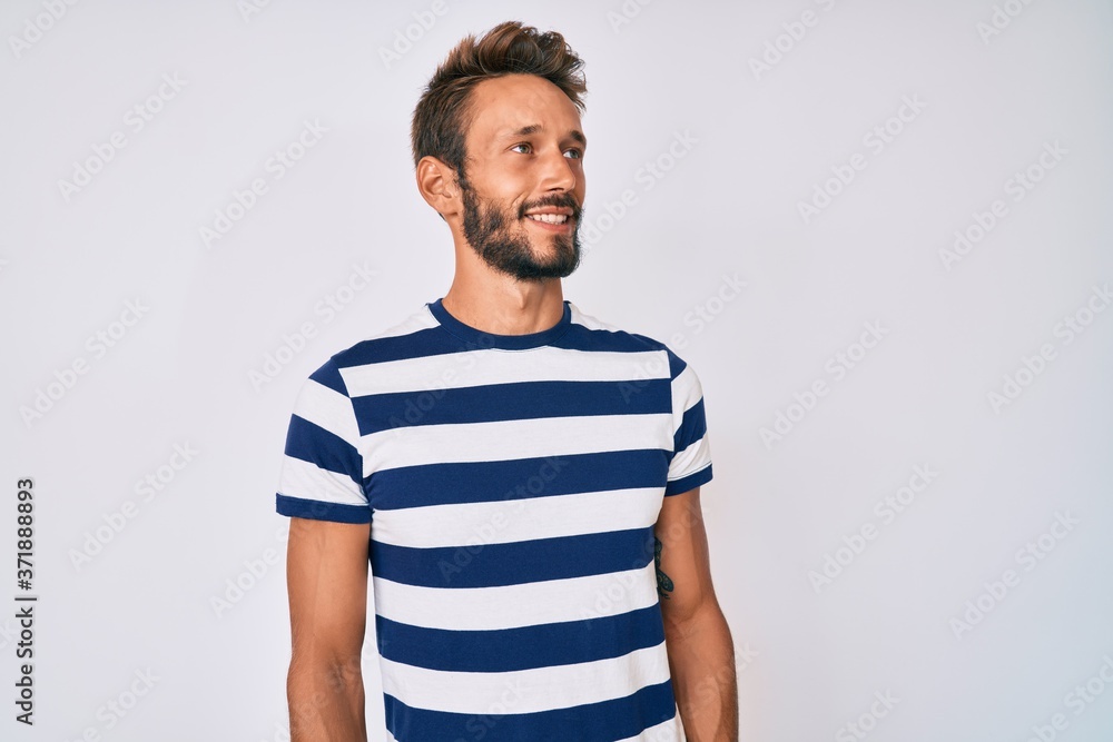 Handsome caucasian man with beard wearing casual striped t-shirt looking away to side with smile on face, natural expression. laughing confident. Handsome caucasian man with beard wearing casual striped t-shirt looking away to side with smile on face, natural expression. laughing confident.
