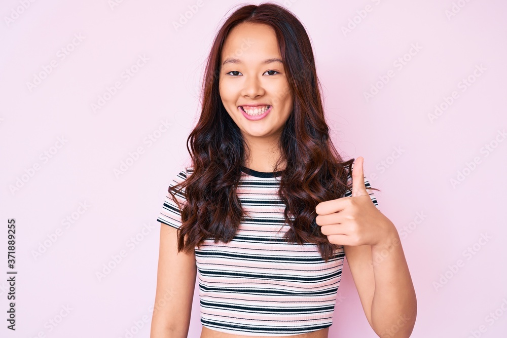 Young beautiful chinese girl wearing casual clothes smiling happy and positive, thumb up doing excellent and approval sign Young beautiful chinese girl wearing casual clothes smiling happy and positive, thumb up doing excellent and approval sign