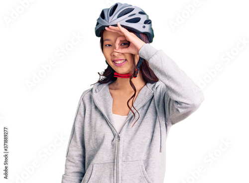 Young beautiful chinese girl wearing bike helmet smiling happy doing ok sign with hand on eye looking through fingers © Krakenimages.com