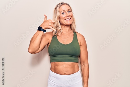 Middle age caucasian blonde woman wearing sportswear smiling doing phone gesture with hand and fingers like talking on the telephone. communicating concepts.