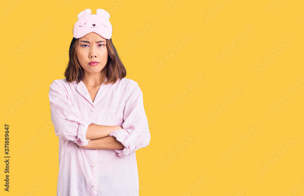 Young beautiful chinese girl wearing sleep mask and pajama skeptic and nervous, disapproving expression on face with crossed arms. negative person. Young beautiful chinese girl wearing sleep mask and pajama skeptic and nervous, disapproving expression on face with crossed arms. negative person.
