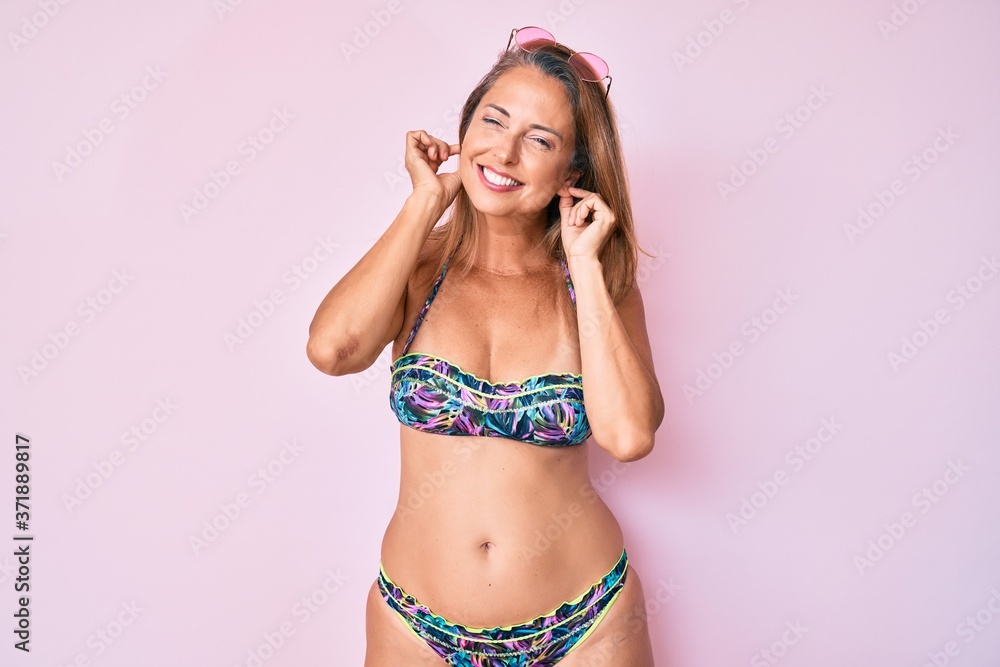 Middle age hispanic woman wearing bikini covering ears with fingers with annoyed expression for the noise of loud music. deaf concept. Middle age hispanic woman wearing bikini covering ears with fingers with annoyed expression for the noise of loud music. deaf concept.