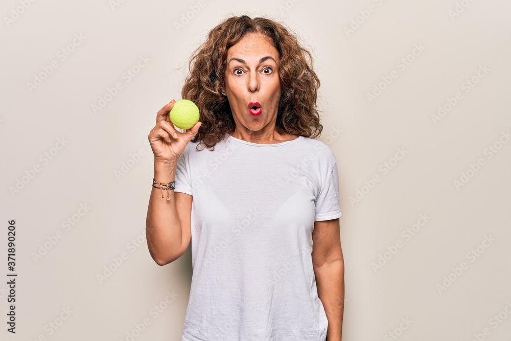 Middle age beautiful sportswoman holding tennis ball over isolated white background scared and amazed with open mouth for surprise, disbelief face Middle age beautiful sportswoman holding tennis ball over isolated white background scared and amazed with open mouth for surprise, disbelief face