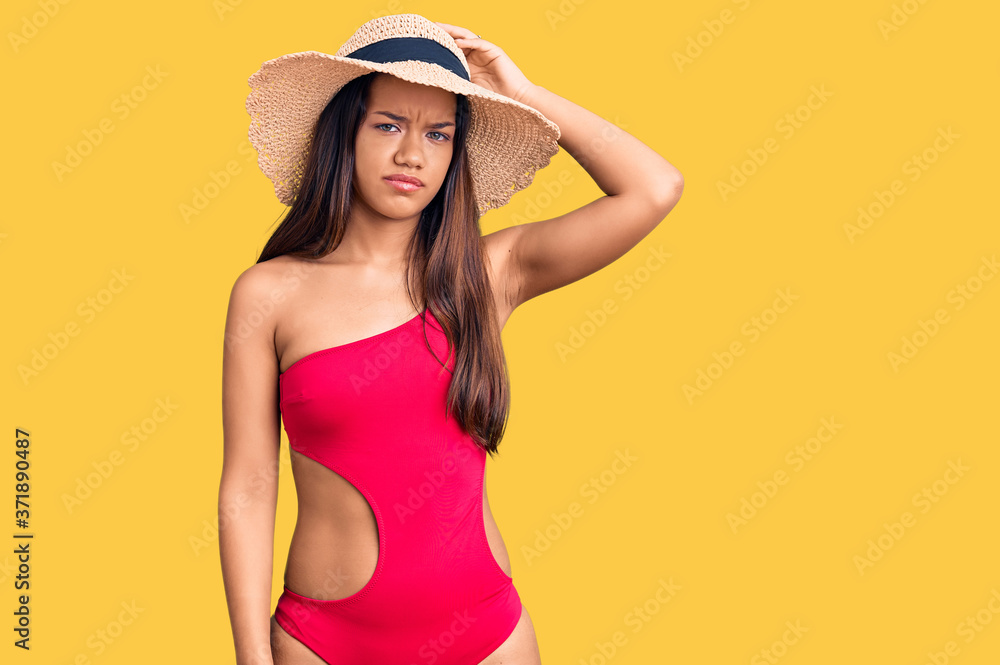 Young beautiful latin girl wearing swimwear and summer hat confuse and wonder about question. uncertain with doubt, thinking with hand on head. pensive concept. Young beautiful latin girl wearing swimwear and summer hat confuse and wonder about question. uncertain with doubt, thinking with hand on head. pensive concept.