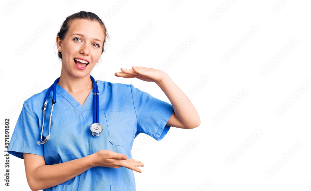 Young beautiful blonde woman wearing doctor uniform and stethoscope gesturing with hands showing big and large size sign, measure symbol. smiling looking at the camera. measuring concept. Young beautiful blonde woman wearing doctor uniform and stethoscope gesturing with hands showing big and large size sign, measure symbol. smiling looking at the camera. measuring concept.