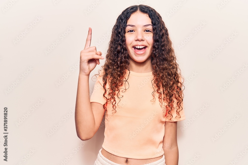 Beautiful kid girl with curly hair wearing casual clothes pointing finger up with successful idea. exited and happy. number one.