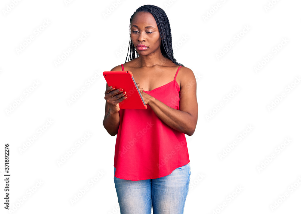 Young african american woman holding touchpad thinking attitude and sober expression looking self confident Young african american woman holding touchpad thinking attitude and sober expression looking self confident