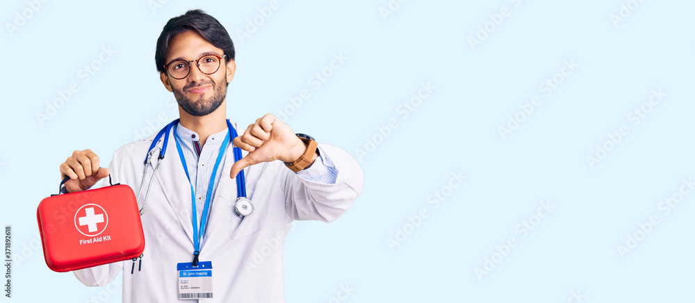 Handsome hispanic man wearing doctor coat holding first aid kit with angry face, negative sign showing dislike with thumbs down, rejection concept Handsome hispanic man wearing doctor coat holding first aid kit with angry face, negative sign showing dislike with thumbs down, rejection concept