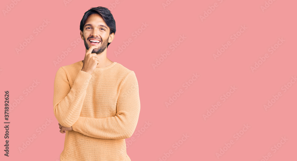 Handsome hispanic man wearing casual sweater looking confident at the camera with smile with crossed arms and hand raised on chin. thinking positive. Handsome hispanic man wearing casual sweater looking confident at the camera with smile with crossed arms and hand raised on chin. thinking positive.