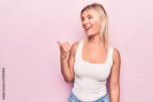 Wallpaper Mural Young beautiful blonde woman wearing casual t-shirt standing over isolated pink background pointing thumb up to the side smiling happy with open mouth Torontodigital.ca